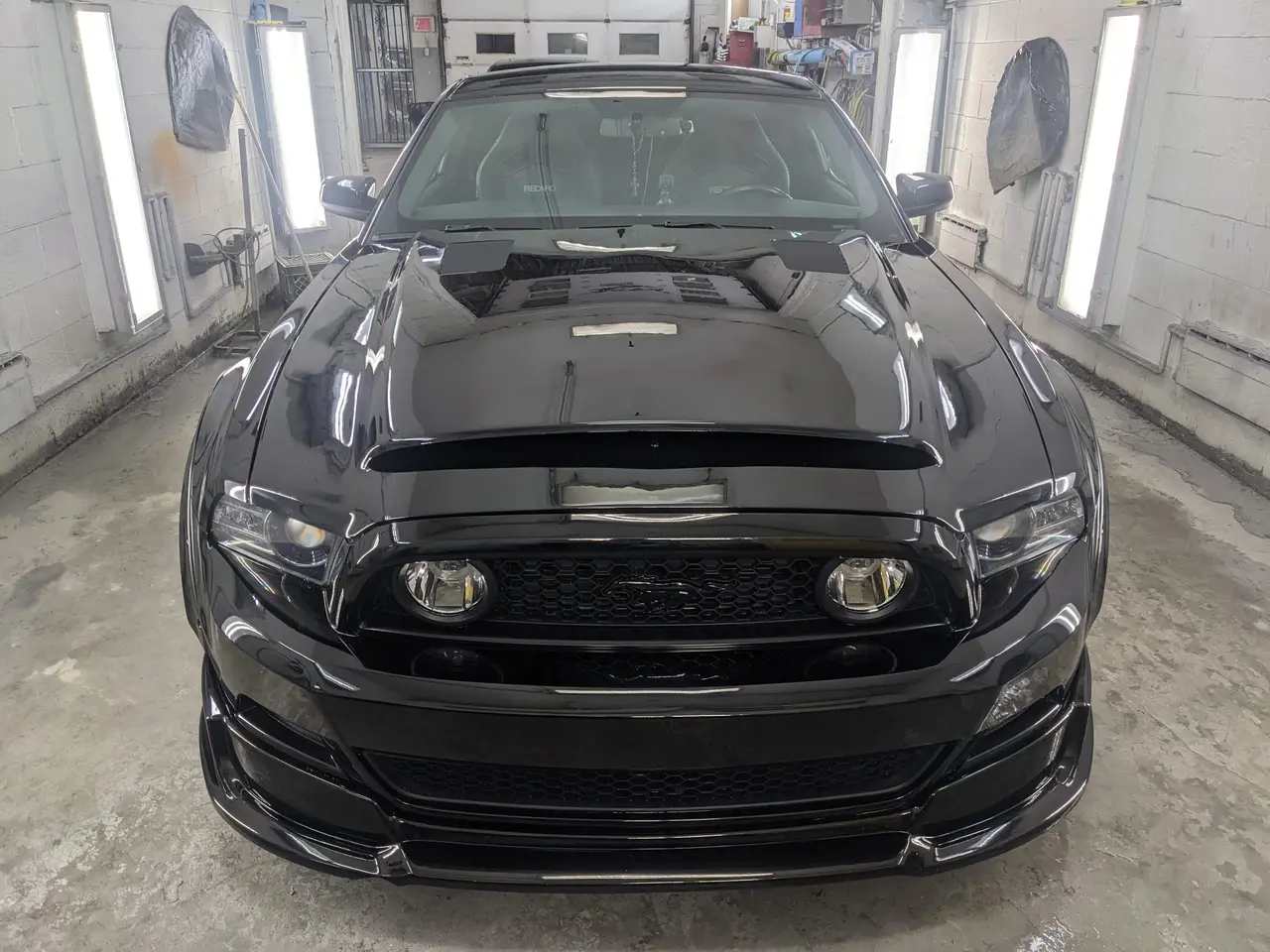 Ford Mustang GT noire vue de face dans la cabine de peinture