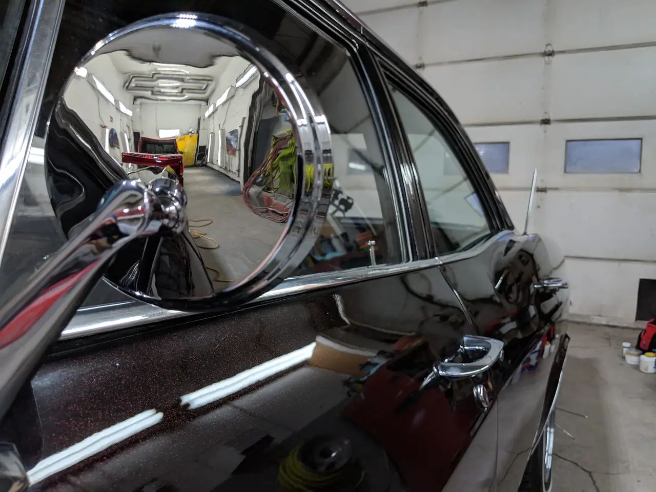 Rétroviseur chromé d’une voiture classique bordeaux, l’atelier se reflétant dans le miroir