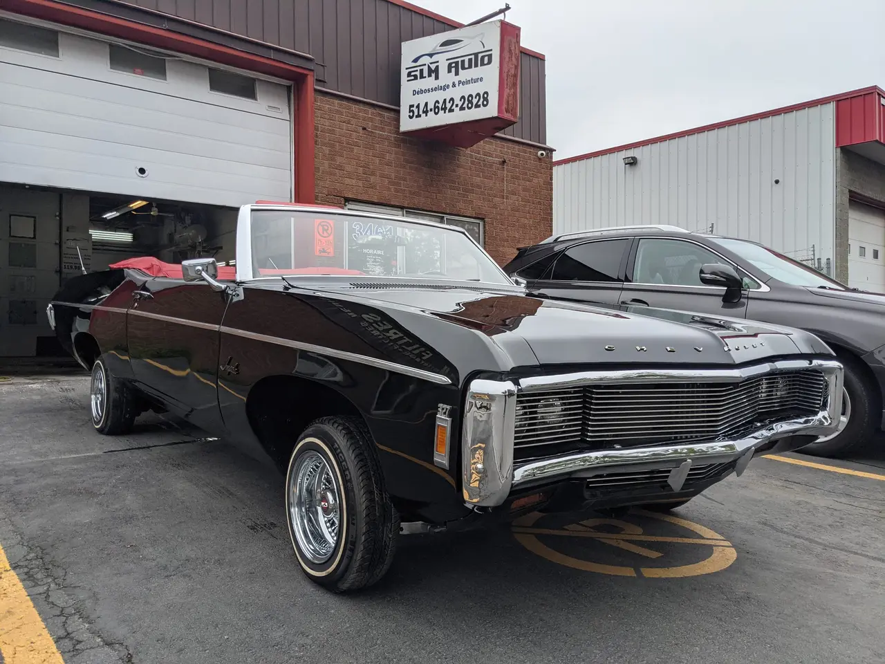 Chevrolet Impala décapotable noire à intérieur rouge, devant l’enseigne de SLM Auto