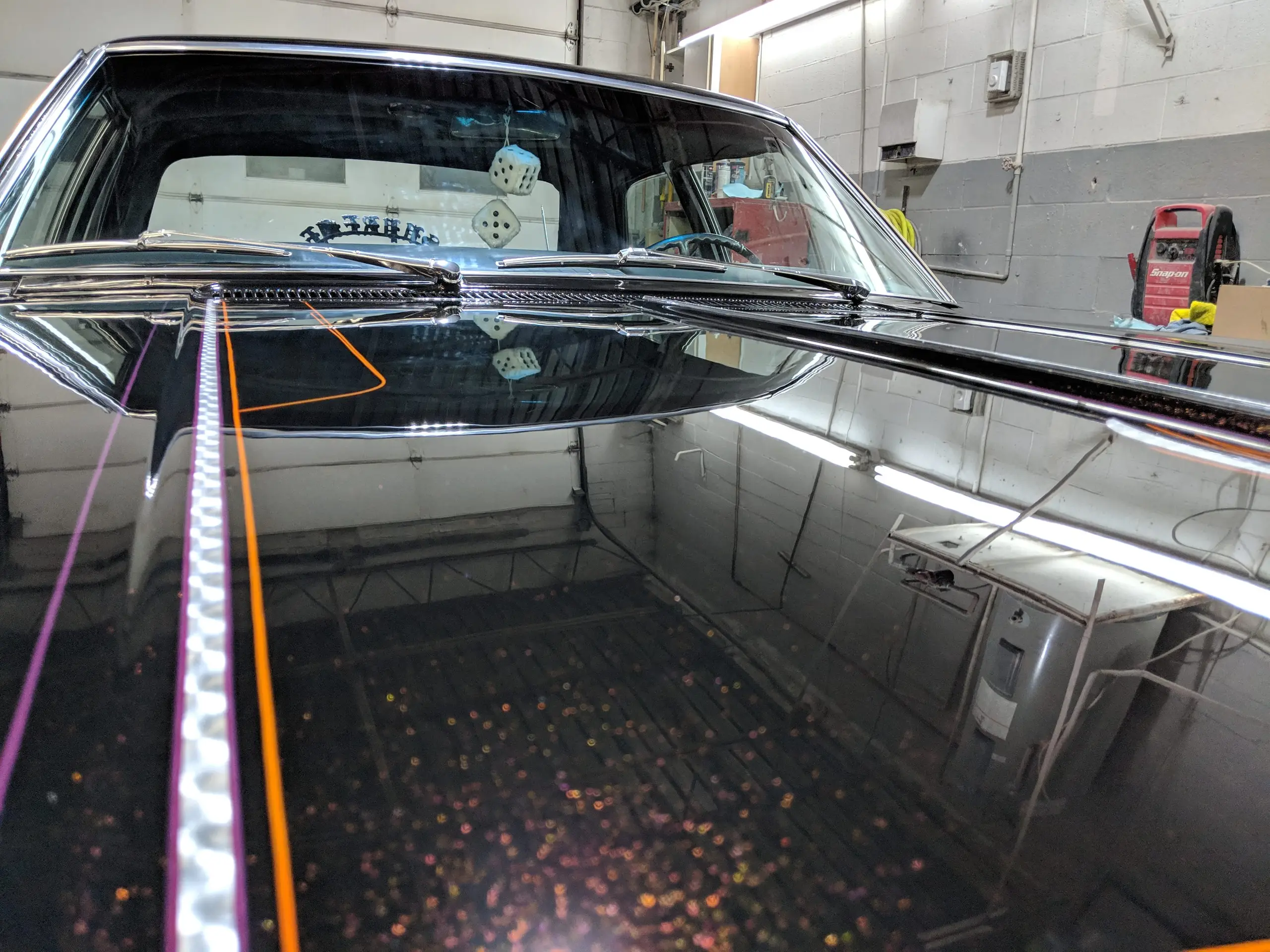 Filet orange et violet longeant le capot noir d’une voiture classique, la lumière révélant la ligne