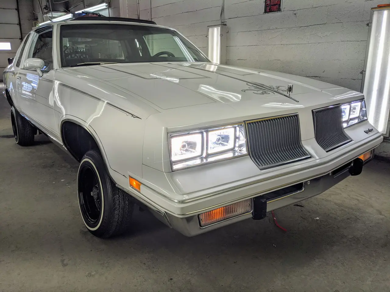 Oldsmobile Cutlass blanche, trois quarts avant, dans l’atelier SLM Auto